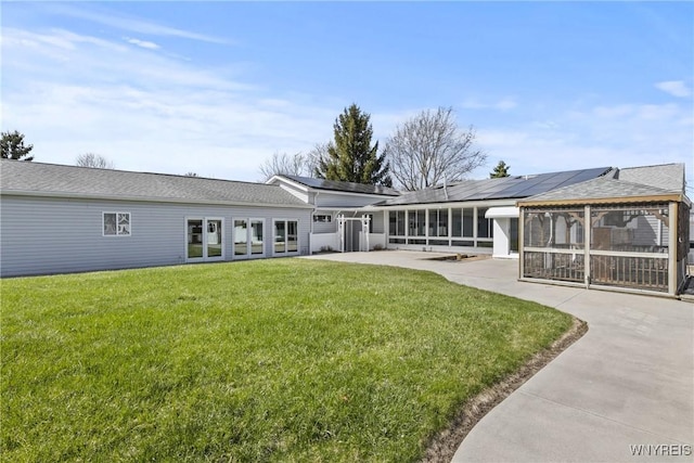 back of house with an attached garage, a lawn, roof mounted solar panels, a sunroom, and a patio