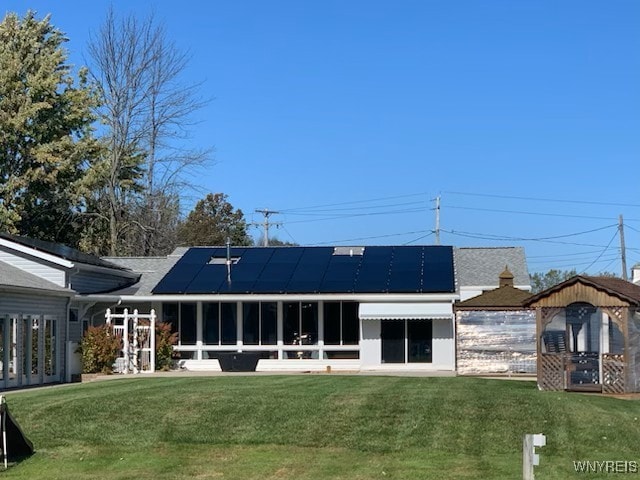 rear view of house with a lawn, roof mounted solar panels, and a sunroom
