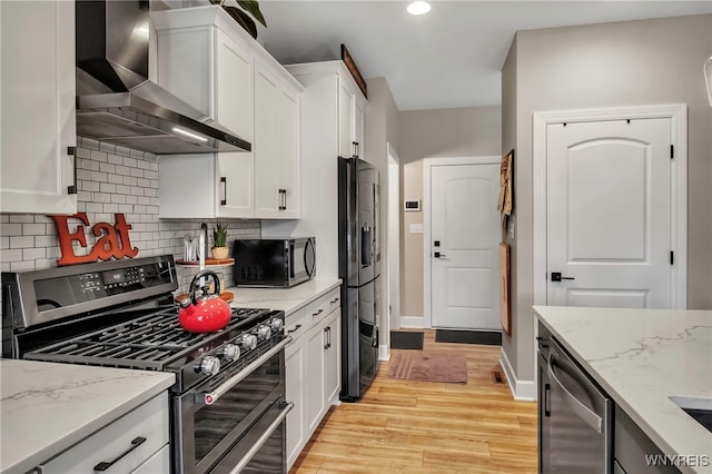 kitchen featuring wall chimney exhaust hood, white cabinets, recessed lighting, decorative backsplash, and appliances with stainless steel finishes