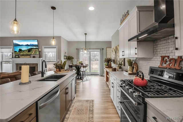 kitchen with stainless steel appliances, backsplash, wall chimney range hood, a sink, and light wood-style floors