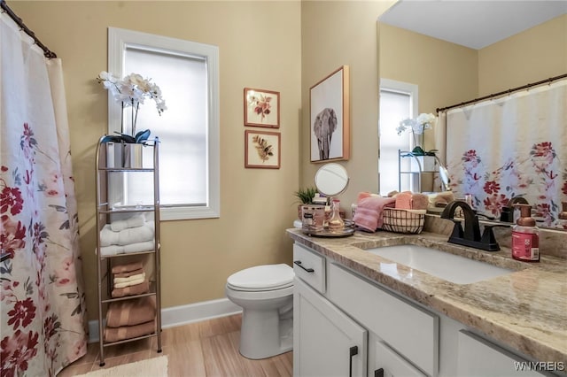 bathroom with baseboards, wood finished floors, toilet, and vanity
