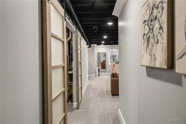 hall featuring light colored carpet, a barn door, and baseboards