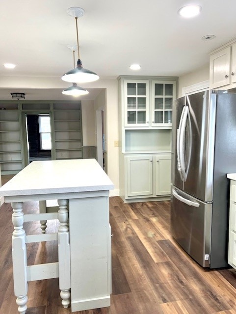 kitchen with light countertops, freestanding refrigerator, glass insert cabinets, hanging light fixtures, and dark wood-style flooring