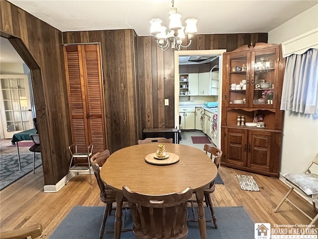 dining area featuring wooden walls, light wood-style floors, and an inviting chandelier