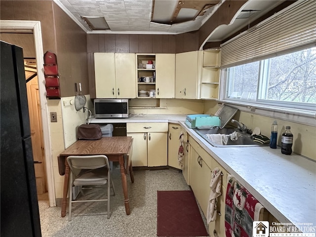 kitchen featuring stainless steel microwave, freestanding refrigerator, cream cabinetry, open shelves, and light countertops