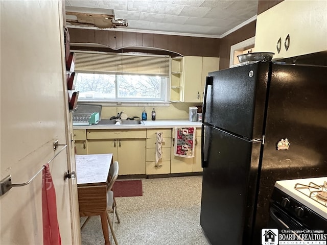 kitchen featuring cream cabinetry, light countertops, a sink, freestanding refrigerator, and crown molding