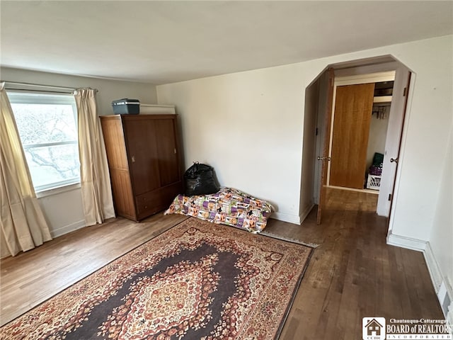 bedroom featuring arched walkways, baseboards, and wood finished floors