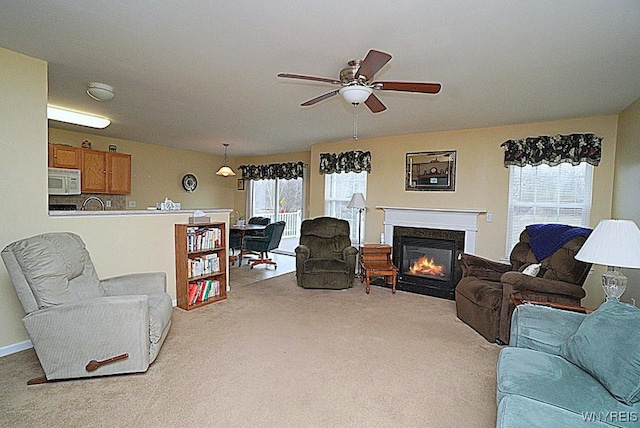 living area featuring a glass covered fireplace, a wealth of natural light, a ceiling fan, and light carpet