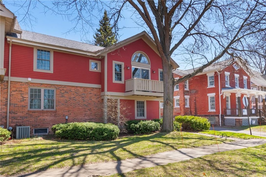 rear view of property featuring central air condition unit, brick siding, and a lawn