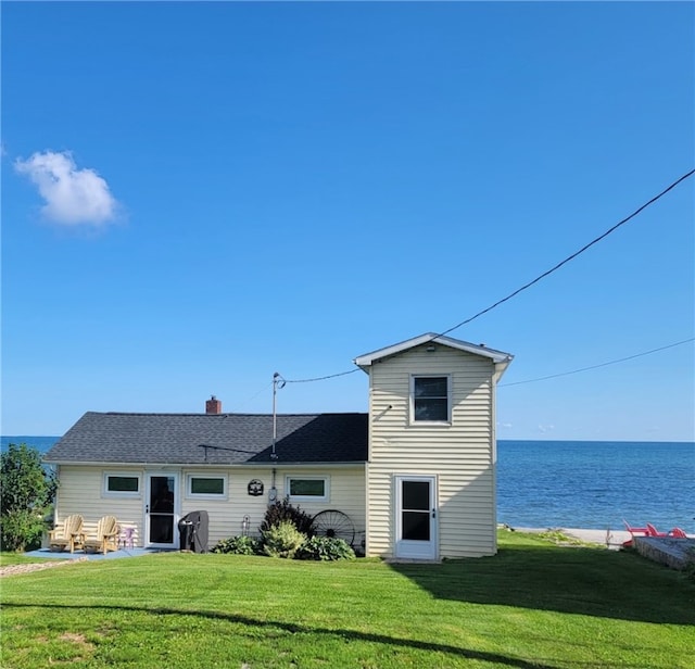 back of house featuring a lawn, a water view, and a chimney