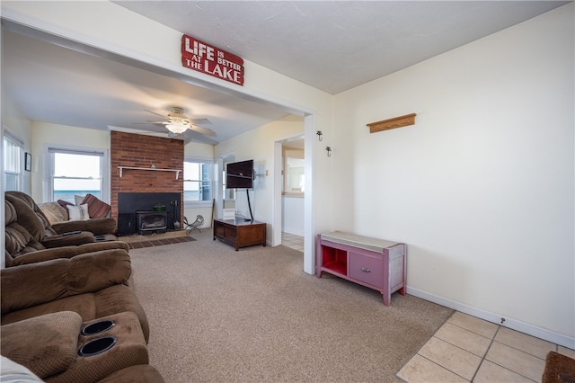 living room with a wood stove, light carpet, light tile patterned flooring, baseboards, and ceiling fan
