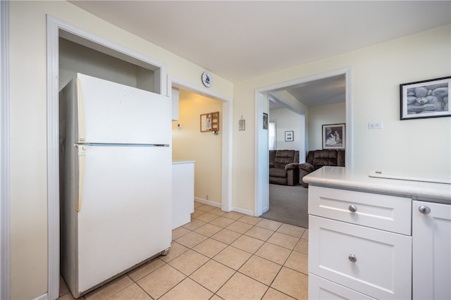 kitchen featuring white cabinets, light tile patterned flooring, freestanding refrigerator, light colored carpet, and light countertops