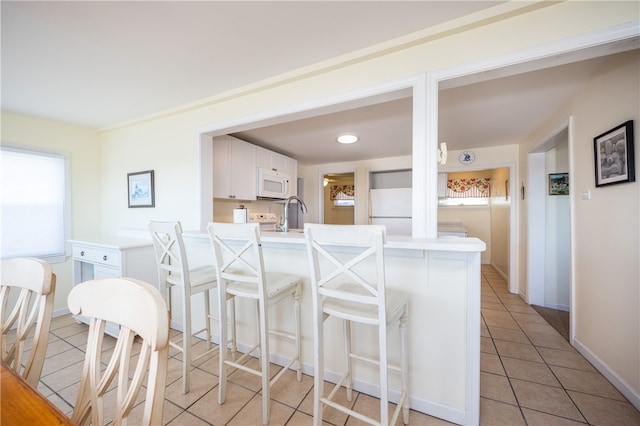 kitchen with a peninsula, a kitchen breakfast bar, white appliances, light countertops, and light tile patterned floors