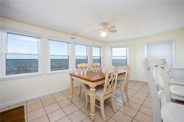 dining space with a water view, baseboards, ceiling fan, and light tile patterned floors