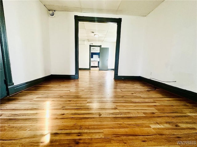 empty room featuring a paneled ceiling, baseboards, and wood finished floors