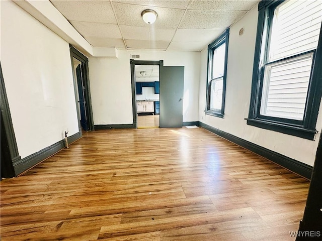empty room with baseboards, light wood-style flooring, and a paneled ceiling