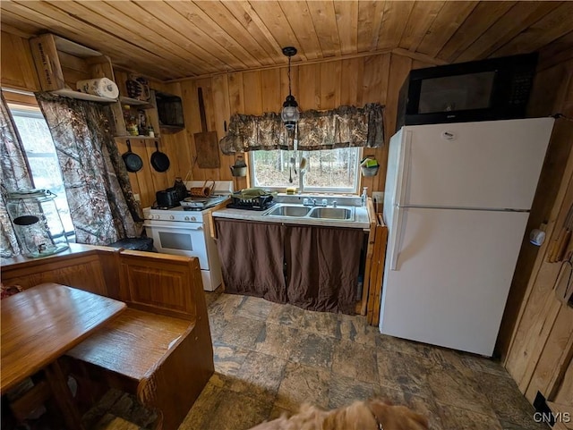 kitchen with a sink, wooden walls, white appliances, wood ceiling, and stone finish flooring