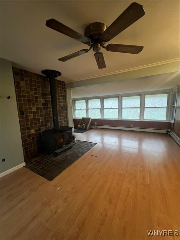 living area featuring a ceiling fan, wood finished floors, a wood stove, baseboards, and ornamental molding
