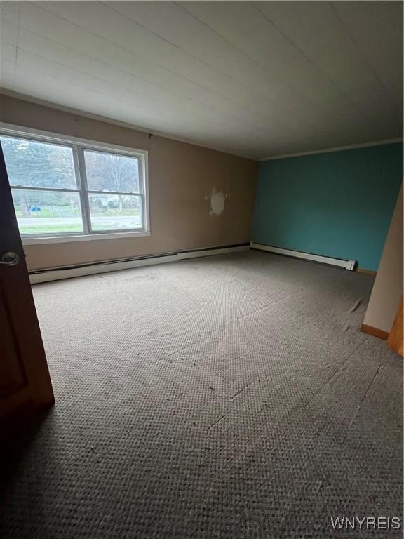 empty room featuring a baseboard heating unit, carpet floors, and baseboards