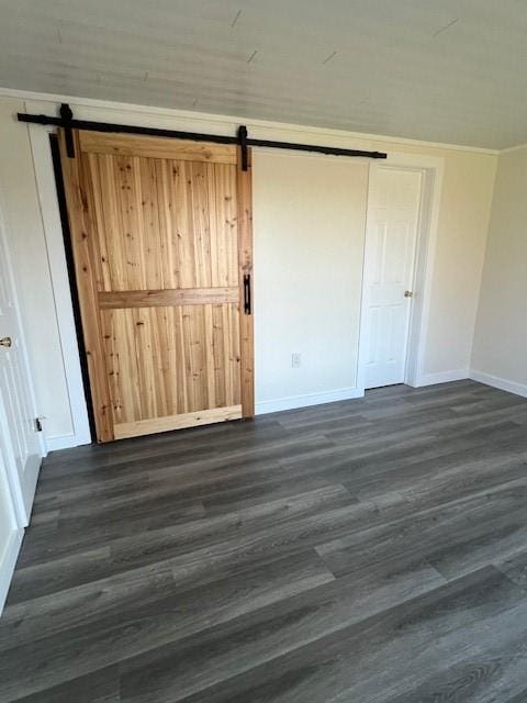 empty room featuring baseboards, dark wood finished floors, and a barn door