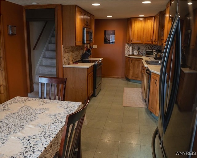 kitchen featuring stainless steel microwave, decorative backsplash, brown cabinetry, freestanding refrigerator, and electric range
