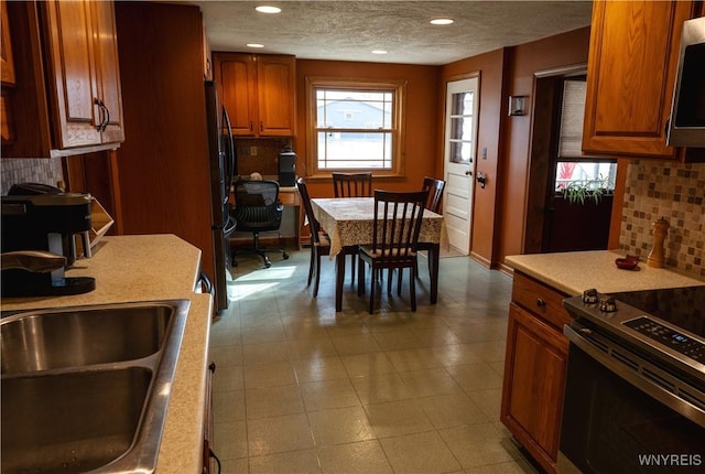 kitchen with decorative backsplash, brown cabinetry, appliances with stainless steel finishes, light countertops, and a sink