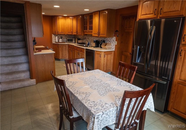 kitchen featuring tasteful backsplash, glass insert cabinets, brown cabinetry, black appliances, and a sink