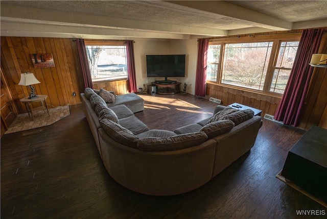 living room with beam ceiling, dark wood-type flooring, visible vents, wood walls, and a textured ceiling