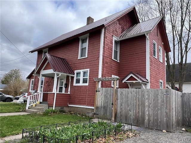 view of front of property with a chimney, metal roof, and fence