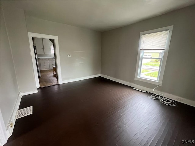 spare room featuring baseboards, visible vents, and dark wood-style floors