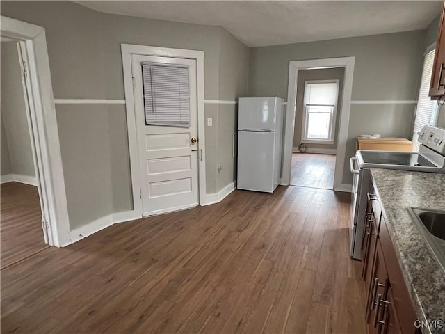 kitchen with baseboards, dark wood-style flooring, dark brown cabinets, and white appliances