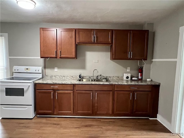 kitchen with white range with electric cooktop, light wood-type flooring, brown cabinetry, and a sink