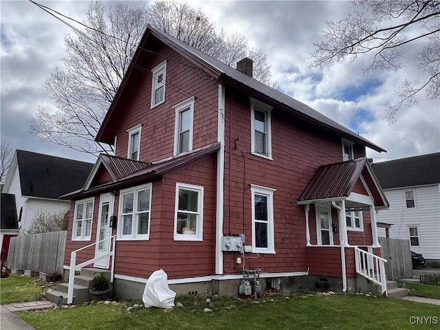 view of front facade with a front yard, entry steps, a chimney, and fence