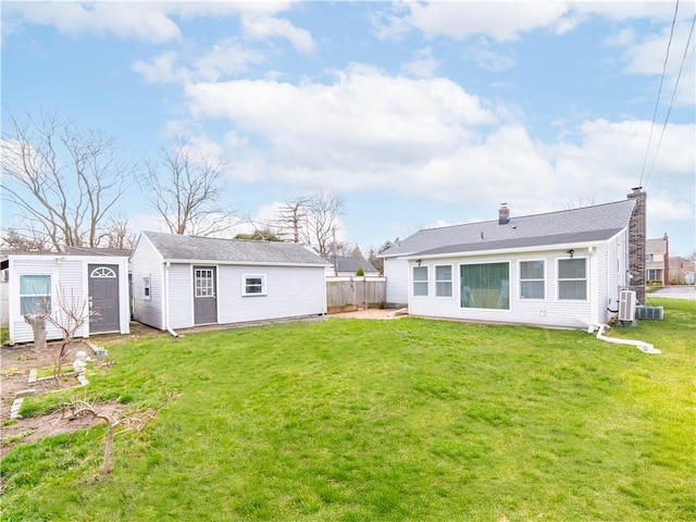rear view of property with a yard, an outbuilding, central AC, and fence