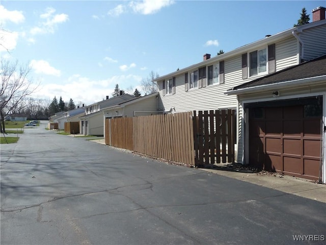view of side of home featuring fence, a chimney, a residential view, and a garage