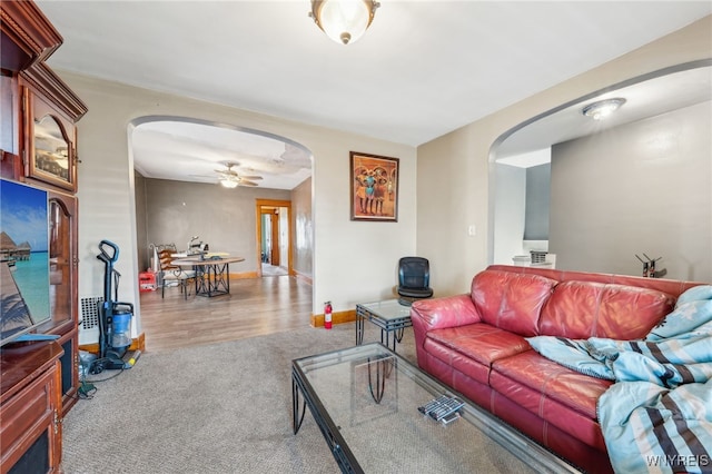 carpeted living area featuring a ceiling fan, baseboards, and arched walkways