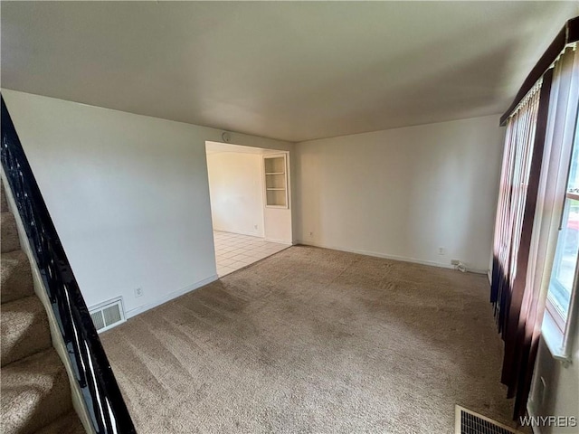 carpeted empty room with baseboards, visible vents, and stairs