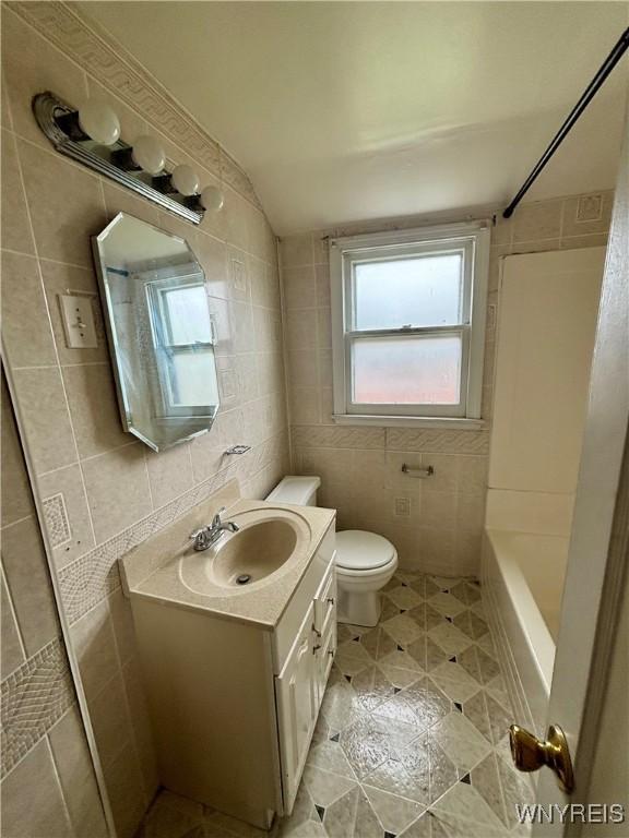 full bathroom with tile patterned floors, toilet, vanity, tub / shower combination, and tile walls