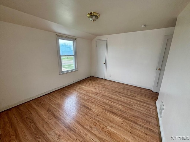 unfurnished room with vaulted ceiling, light wood-type flooring, visible vents, and baseboards