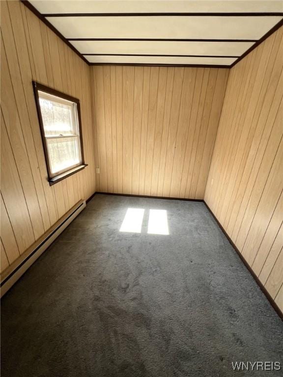 carpeted spare room featuring wood walls and a baseboard radiator