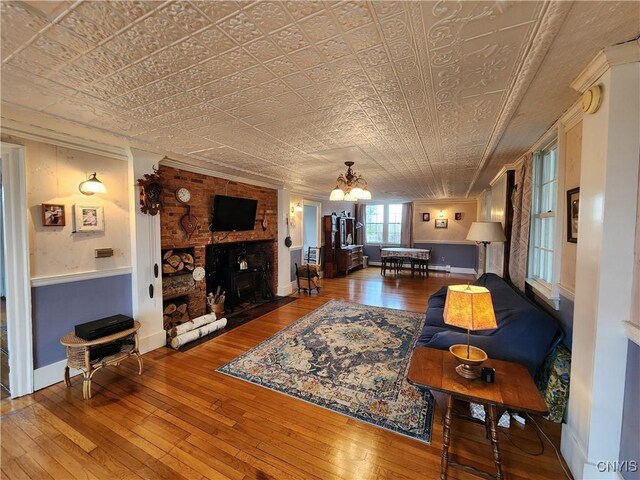 living room with an ornate ceiling, a chandelier, a fireplace, wood-type flooring, and baseboards
