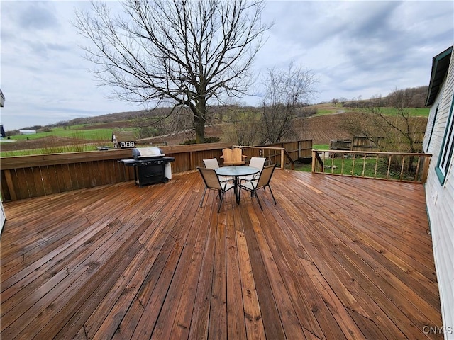 deck featuring a rural view, outdoor dining space, a fenced backyard, and a grill