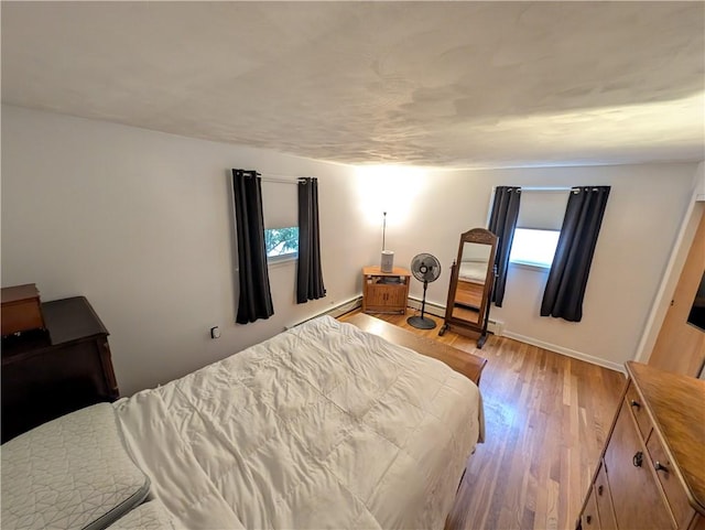 bedroom with a baseboard heating unit, baseboards, and light wood-style flooring