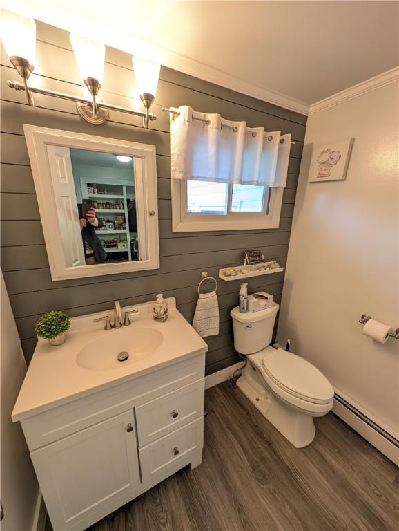 bathroom featuring wood finished floors, a baseboard heating unit, vanity, toilet, and ornamental molding