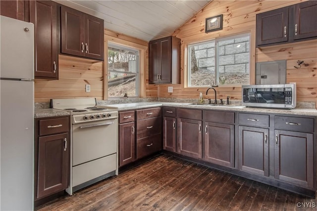 kitchen featuring vaulted ceiling, a sink, wooden walls, white appliances, and dark wood-style floors