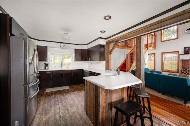 kitchen featuring a sink, stainless steel fridge with ice dispenser, light countertops, a peninsula, and dark wood-type flooring