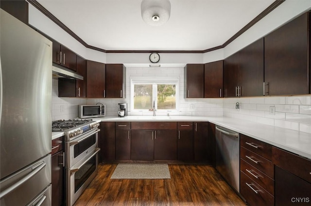 kitchen with under cabinet range hood, stainless steel appliances, light countertops, a sink, and dark wood-style flooring