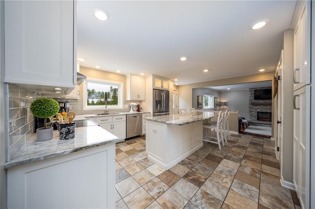kitchen with backsplash, a sink, a kitchen island, a fireplace, and appliances with stainless steel finishes