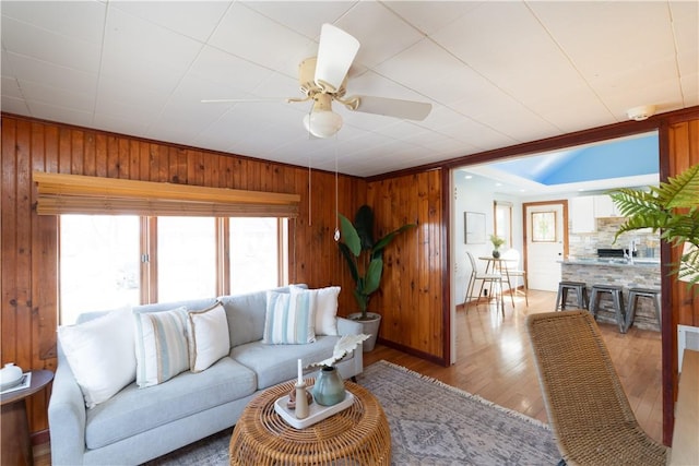 living area with ceiling fan, light wood finished floors, and wooden walls