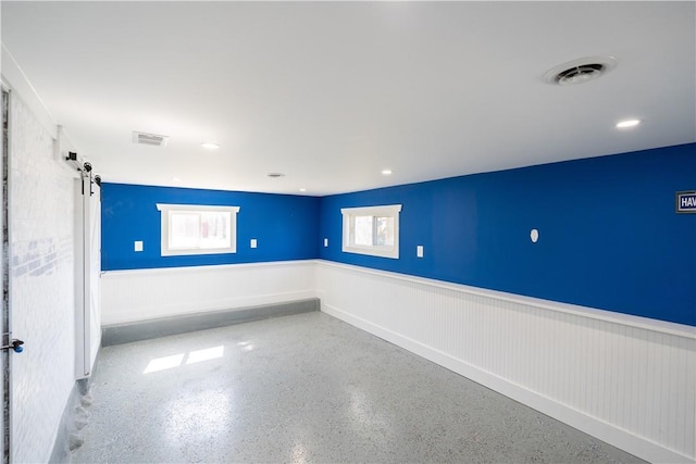 spare room with a barn door, visible vents, and a wainscoted wall